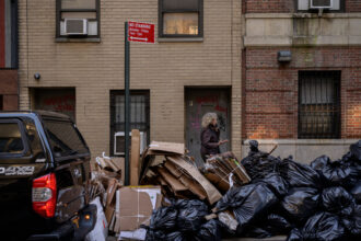 A pedestrians walks by trash bags piled on a street in Manhattan. High Acres gets about 90 percent of its waste by train from New York City. Credit: Ed Jones/AFP via Getty Images