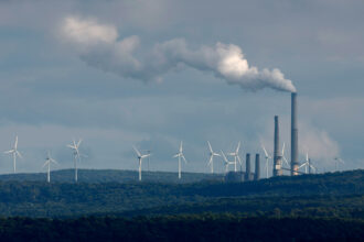 Wind turbines stand in the distance behind Dominion Energy's Mount Storm Power Station in West Virginia. Credit: Chip Somodevilla/Getty Images