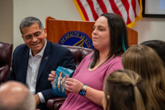 Elizabeth Goldman, an IVF patient, shows a photo of her child during a roundtable with U.S. Health and Human Services Secretary Xavier Becerra on Feb. 27 in Birmingham, Ala. Photo credit: Lee Hedgepeth/ Inside Climate News