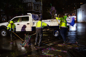 Mobile city workers shovel pounds of Mardi Gras beads into the back of a truck. Credit: Lee Hedgepeth/Inside Climate News