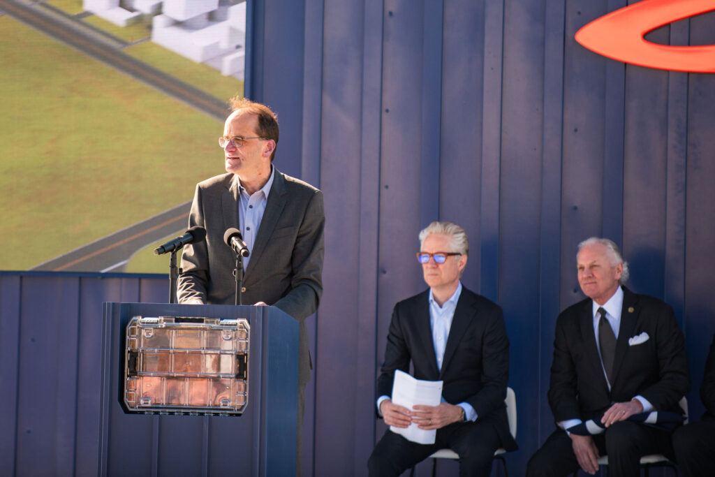 Jan Spies, chief of production at Scout Motors, talks to the crowd gathered at the company's Blythewood, S.C. groundbreaking on Feb. 15. A case at the front of the podium holds a brick from the original Fort Wayne, Ind. Scout factory that will be used in the foundation of the new EV plant. Scout CEO Scott Keogh (left) and South Carolina Gov. Henry McMaster look on. Credit: Scout Motors